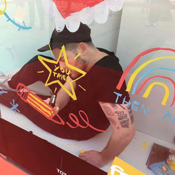 Photo of Adam sitting on the ground, drawing with paint markers onto a glass window.